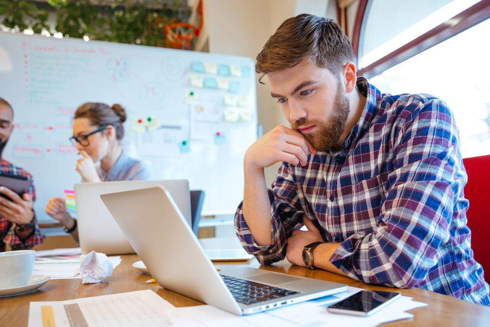 a man working at a laptop with a colleague working in the background